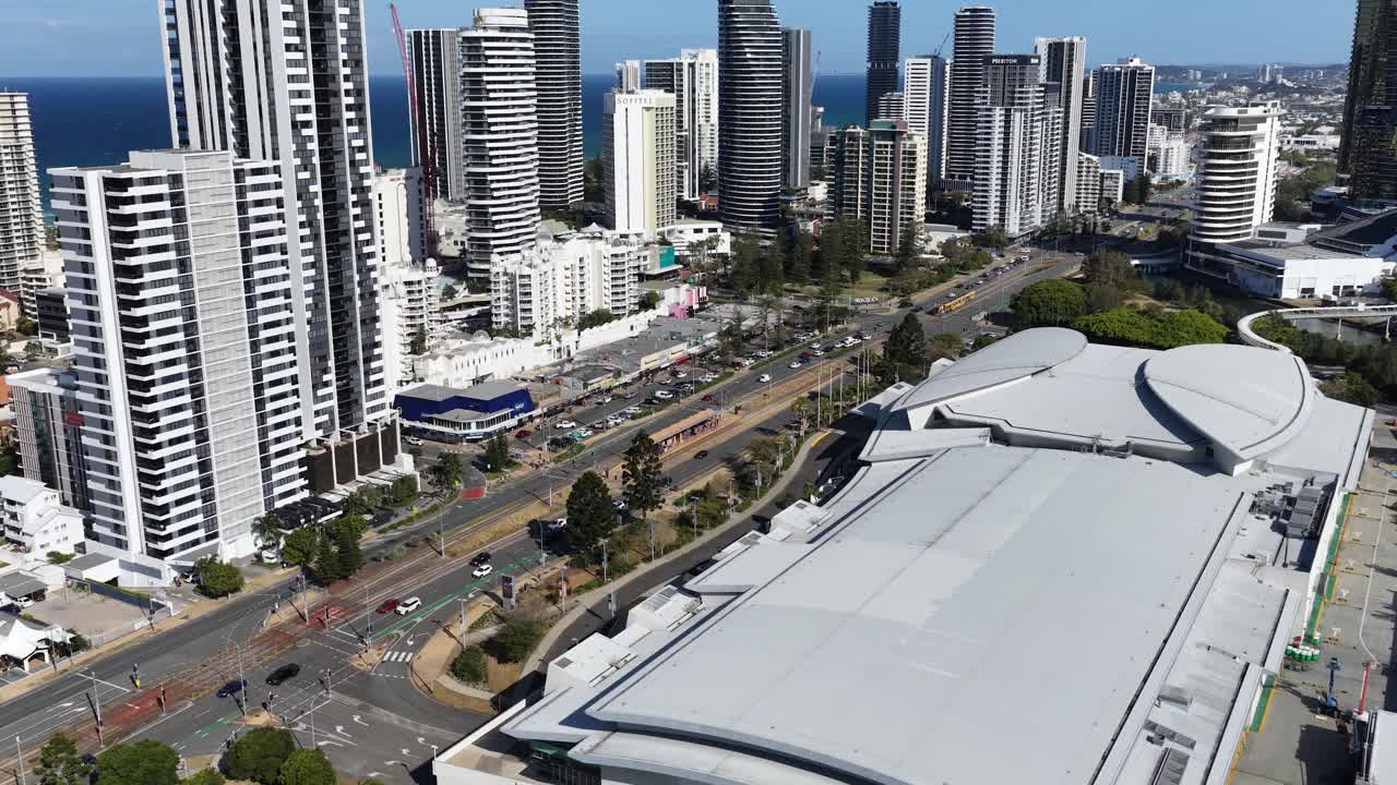 Daytime drone footage glides above convention center, revealing Gold Coast skyscrapers, coastline, and highway