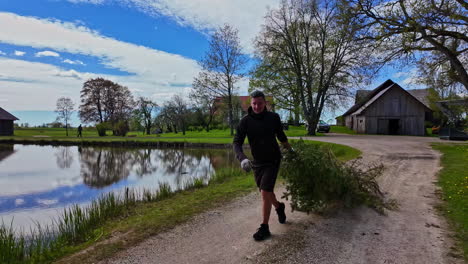 slow motion shot of a man pulling christmas tree beside lake along rural countryside on a cloudy day