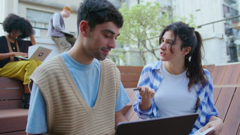 young coworkers using laptop and discussing notes outdoors in the city