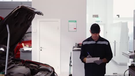 man in uniform in a auto repair shop walking around, making notes on his tablet