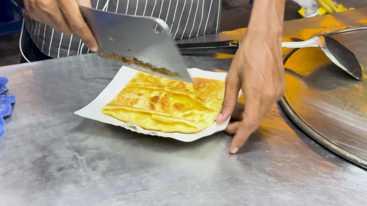 A street vendor skillfully chops Thai roti on a metal surface, showcasing traditional street food preparation in Phuket, Thailand