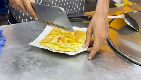 a street vendor skillfully chops thai roti on a metal surface, showcasing traditional street food preparation in phuket, thailand