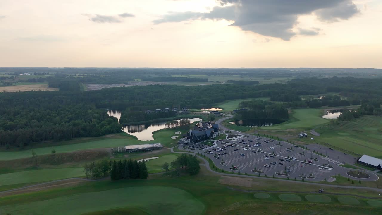 Drone orbit over golf course with trimmed fairways, water traps reflect sky, large open parking lot