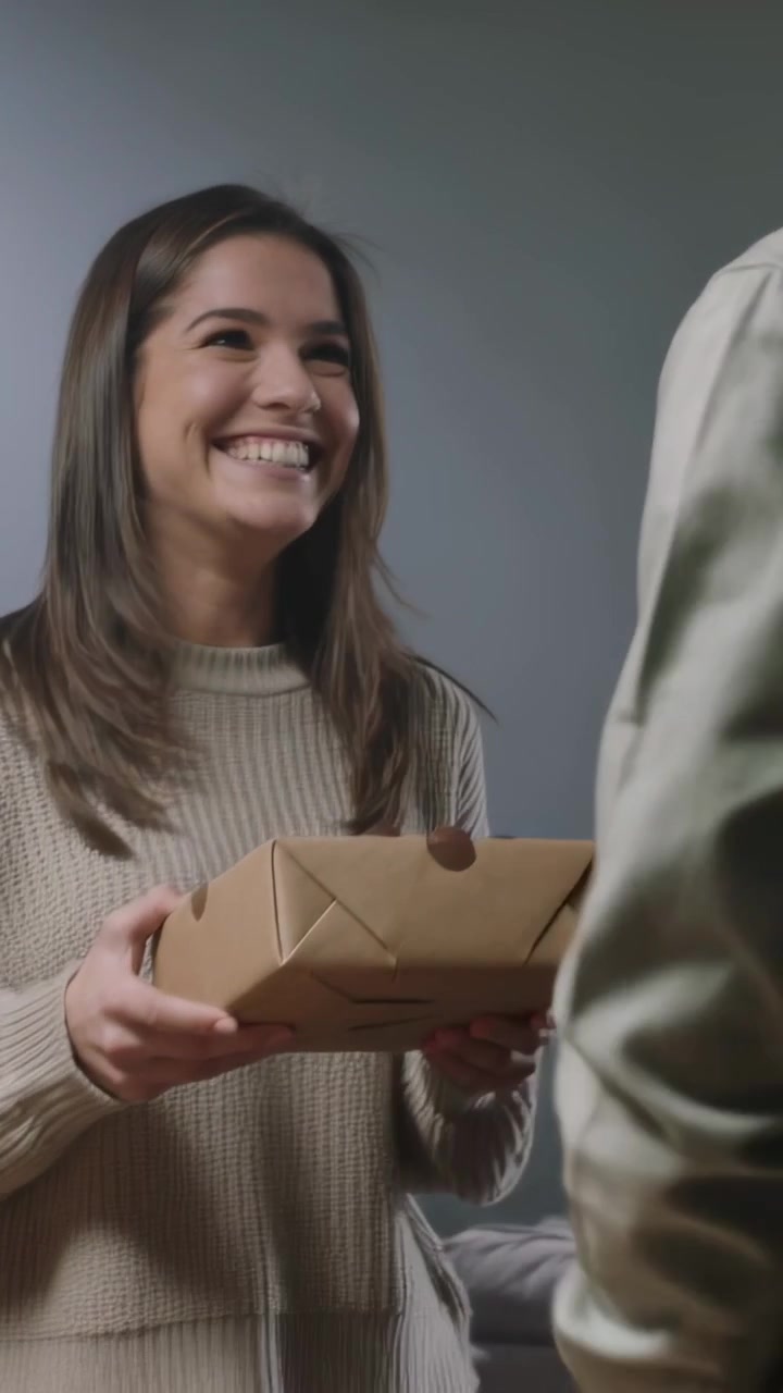 Video verticale: Donna che riceve una scatola marrone dal partner al tavolo come regalo, con un maglione color cammello