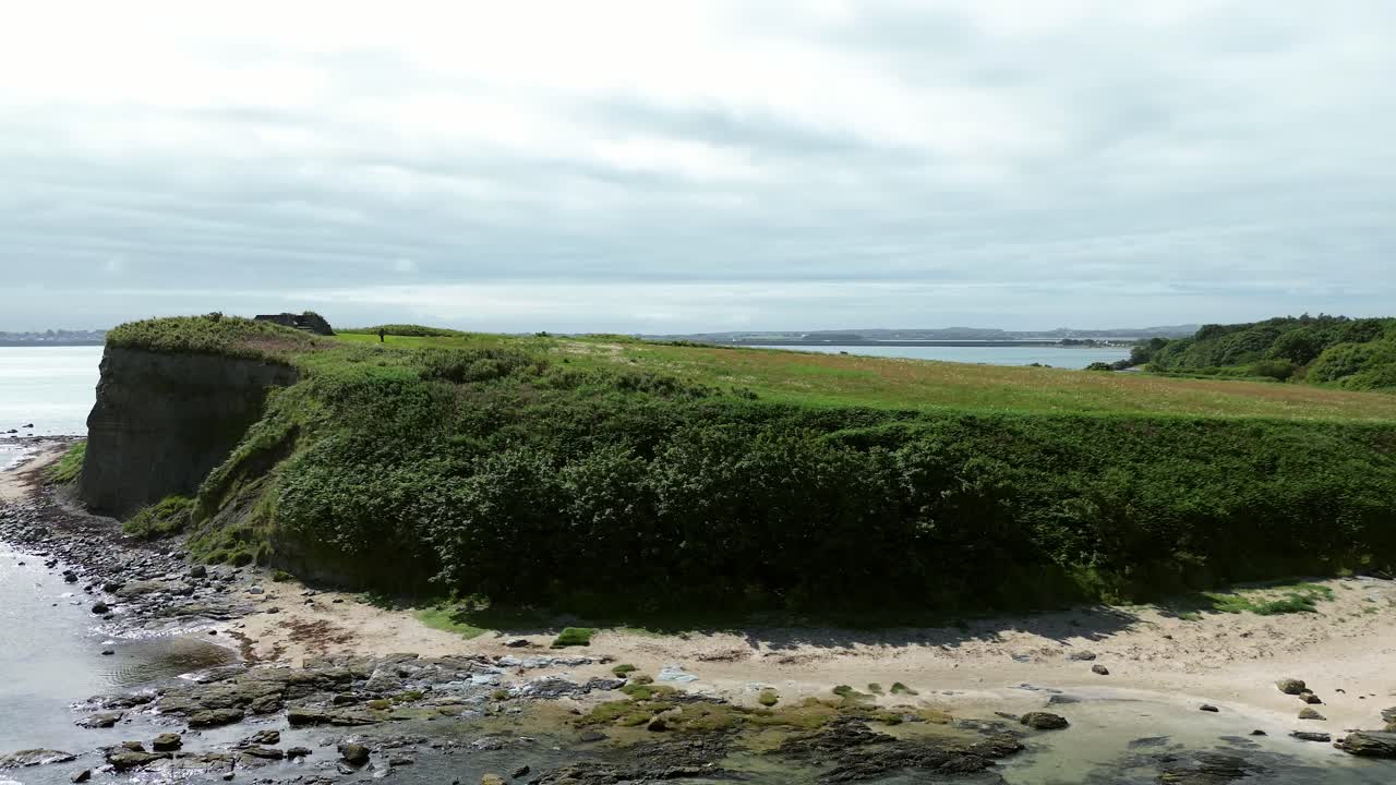 Sunny Welsh coastal Penrhos meadow headland overlooking rocky seafront beach aerial view