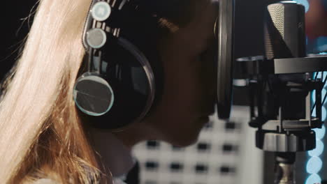 child looks through microphone filter at record studio. naughty little girl plays with audio equipment in music center closeup. kid tired of singing