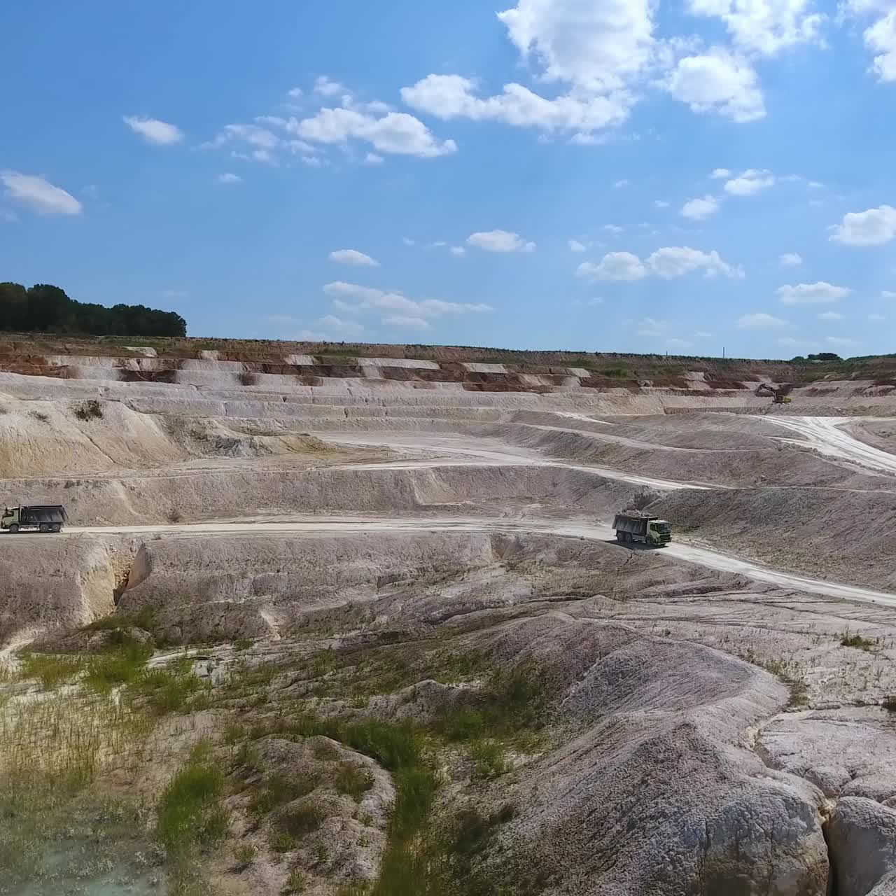 Two trucks meeting at the road through white clay quarry. Hilly white landscape contrasting with the blue skies. Drone shot