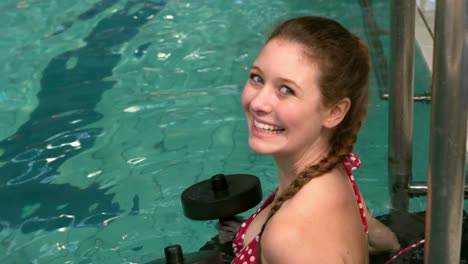 Fit-woman-holding-weights-in-the-pool-and-smiling-at-the-camera