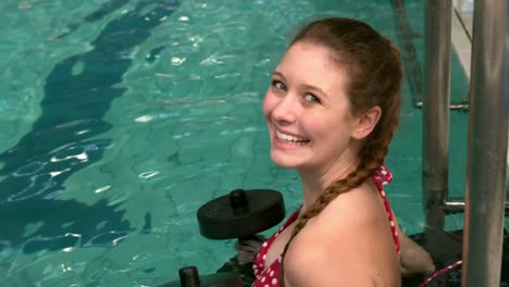 mujer en forma sosteniendo pesas en la piscina y sonriendo a la cámara