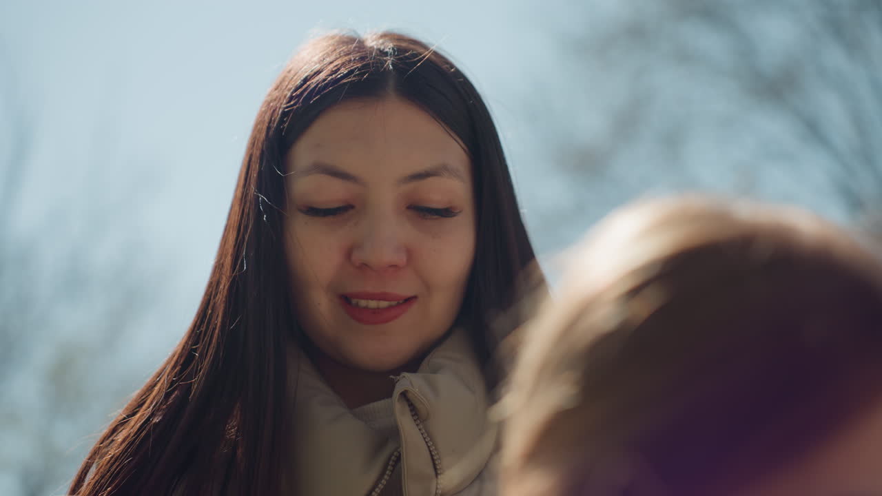 공원 벤치에 앉아 아이에게 몸을 기울인 여성, 부드러운 대화와 다정한 표정, 나무 사이로 비치는 햇빛, 위로와 지지를 제공하는 세심한 보호자, 클로즈업 감성 인물 사진