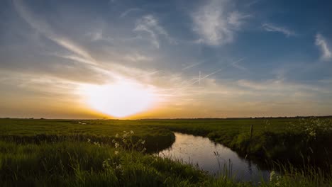 The-movement-of-clouds-over-the-green-field-and-river-at-sunset-in-windy-weather