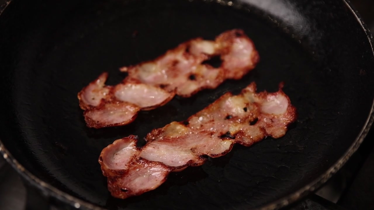 Fette di bacon croccanti che friggono e sfrigolano in una padella calda