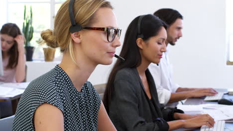 White-woman-in-headset-smiles-to-camera-in-open-plan-office