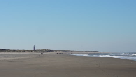 Menschen,-Die-Tagsüber-Am-Strand-Von-Ouddorp-Mit-Dem-Leuchtturm-Westhoofd-In-Der-Ferne-Spazieren-Gehen