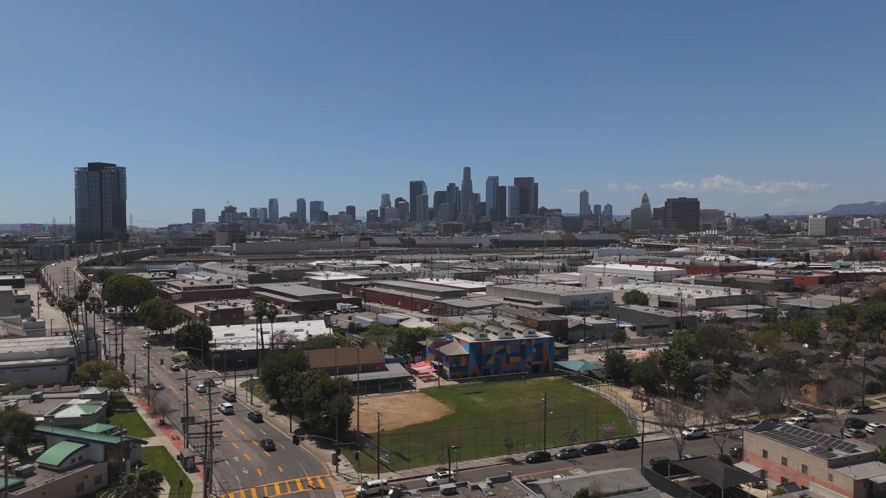 Paesaggio urbano con auto che passano, skyline di Los Angeles in lontananza. Cielo azzurro limpido in una soleggiata giornata californiana. Ripresa aerea panoramica veloce 4K 60FPS