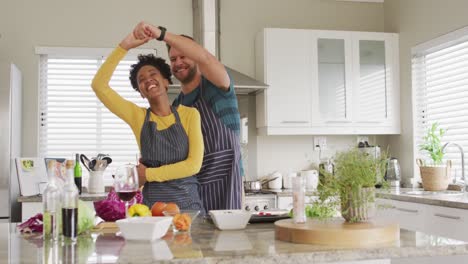 video de una feliz pareja diversa bailando en la cocina con delantales