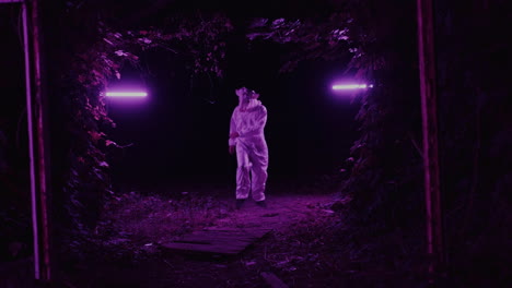 person in white jumpsuit in a purple lit forest at night