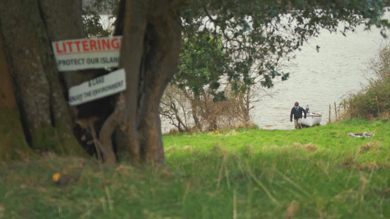 젊은 남자가 섬 해안선에서 보트를 끌어올리고 과거 우리 섬 표지판을 보호합니다.