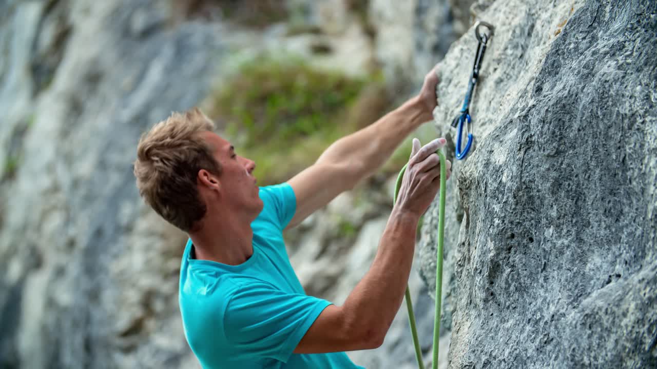 Young strong Caucasian boy rock climber stands, unclips and holds on to mountainside, close up