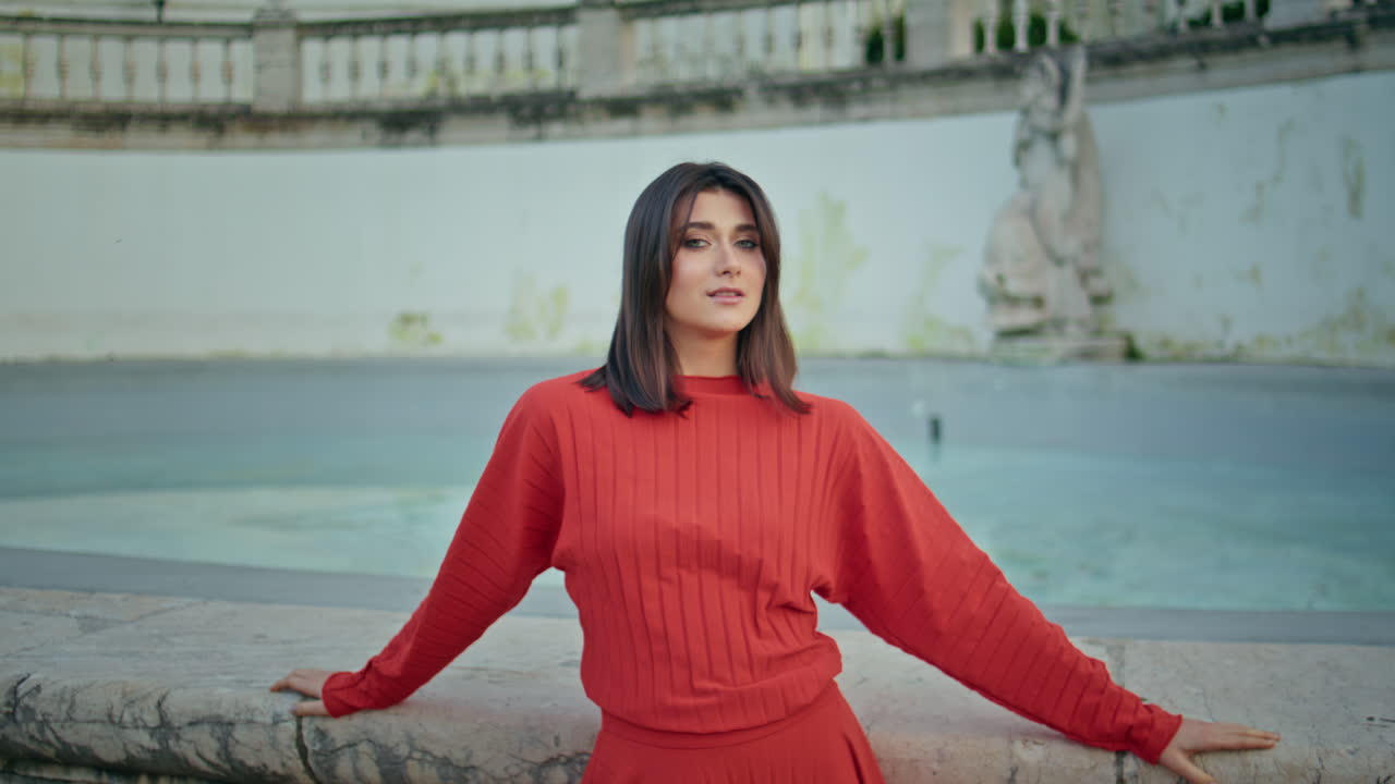 Charming girl posing fountain portrait. Red dress lady looking camera relaxing