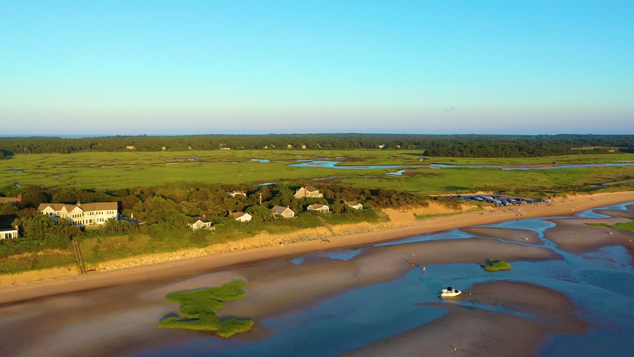 Ripresa aerea con drone di Cape Cod, spiaggia con barriera corallina, scogliera sabbiosa e case costiere vicino a una zona di accesso alla spiaggia molto frequentata, con insenature paludose intrecciate e zone umide sullo sfondo. B-roll sullo stile di vita di viaggio, video 4K cinematografico