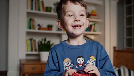 smiling preschooler plays with a small red toy car in his bedroom, enjoying his playtime in a cozy home environment filled with books and plants