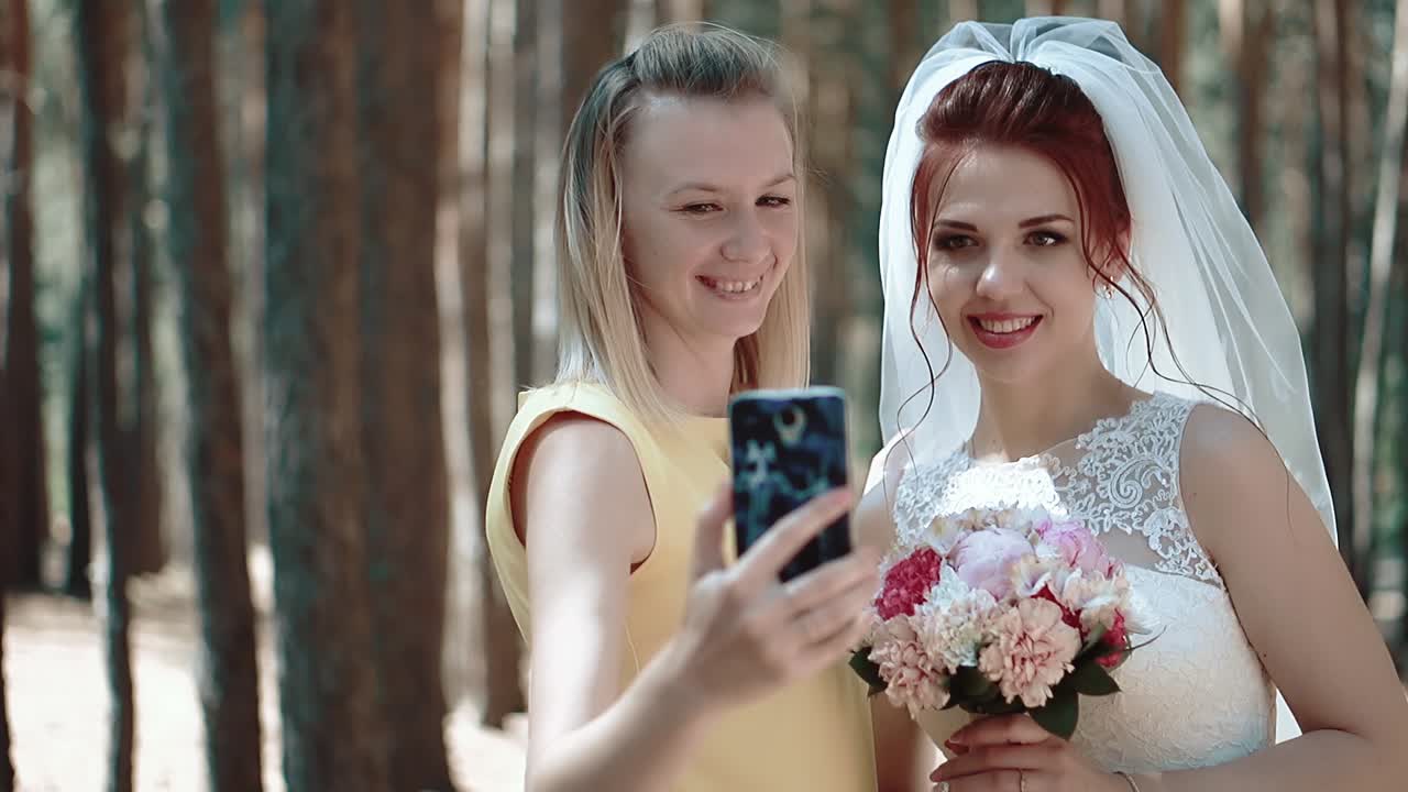 la novia y su amiga se hacen una selfie en el bosque el viento desarrolla su cabello de cerca