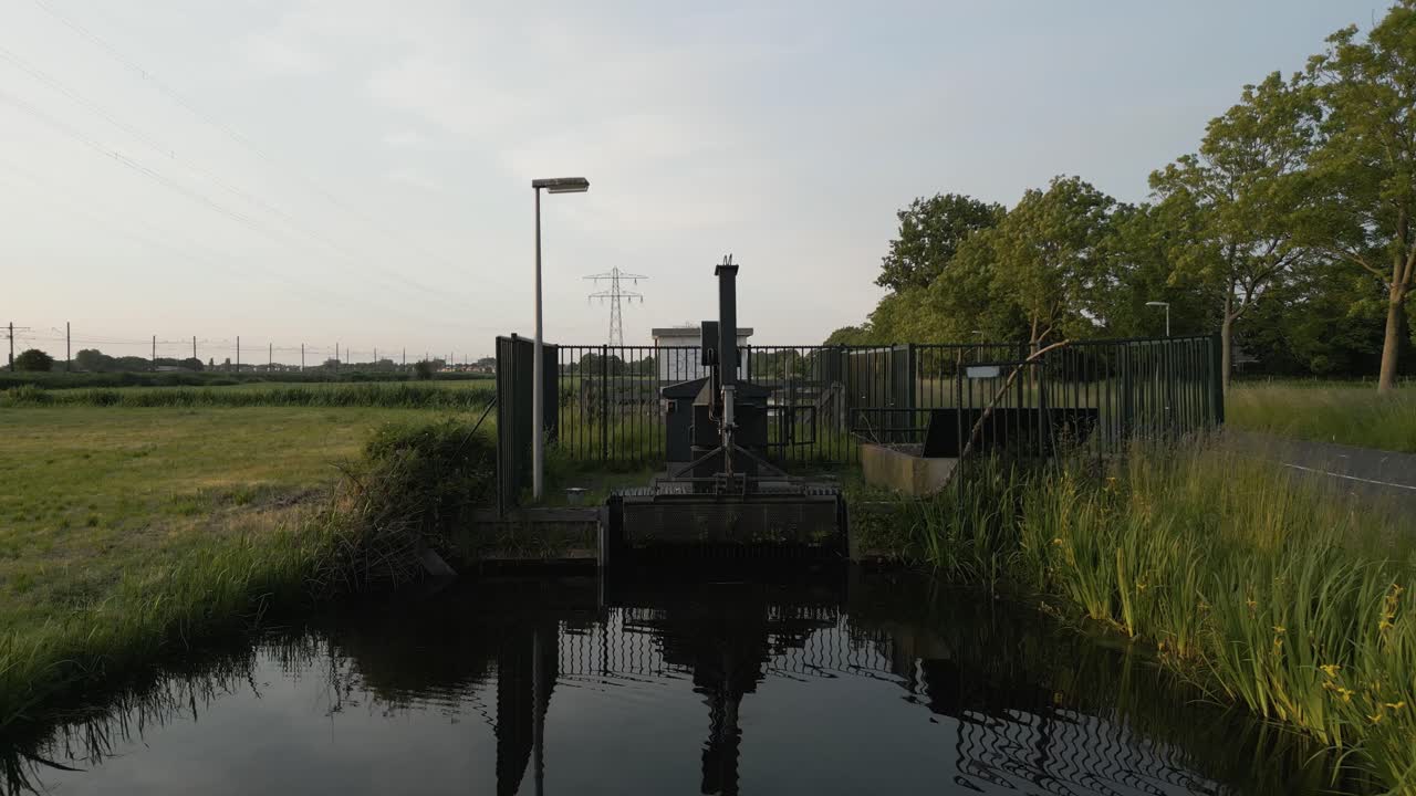 Aerial shot of a small water gate installation in the Dutch countryside, reflecting in calm waters.