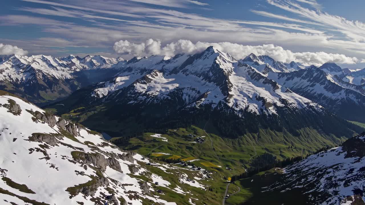 Aerial video of snow-capped mountains under a blue sky with clouds, showcasing a breathtaking