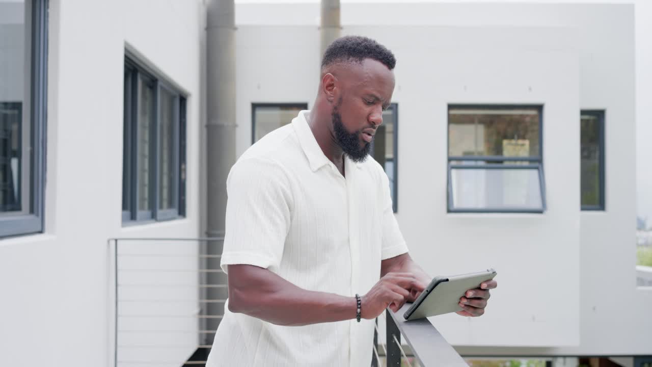 Adult African man is bringing hand forward and tapping tablet on balcony railing to check messages