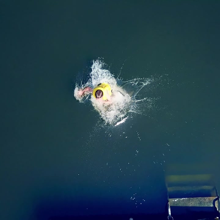 Close-up of a little kid jumping into the water from the old wooden bridge. Young boy in yellow vest dives into the river in summer. Motion camera bottom up