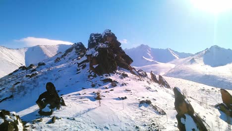 Beautiful-bird's-eye-view-of-winter-rocks-with-snowy-mountains-and-sunny-blue-sky-in-the-background