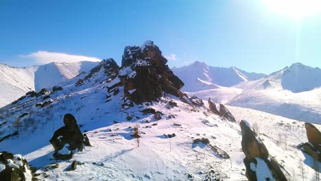 hermosa vista de pájaro de las rocas de invierno con montañas nevadas y cielo azul soleado en el fondo