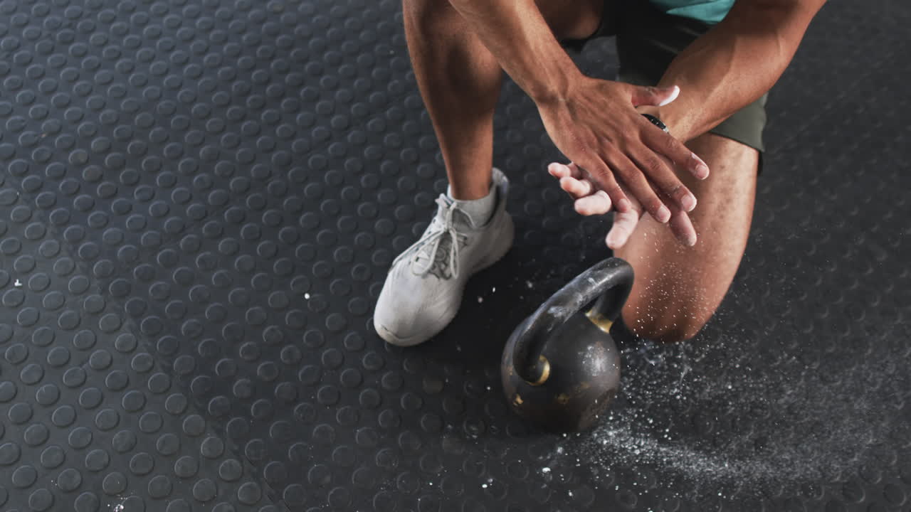 Lifting kettlebell, man clapping hands with chalk in gym workout session