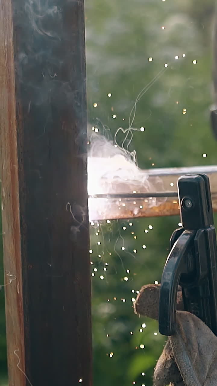 slow motion backside view repairman in mask works at fence building using weld instrument in yard