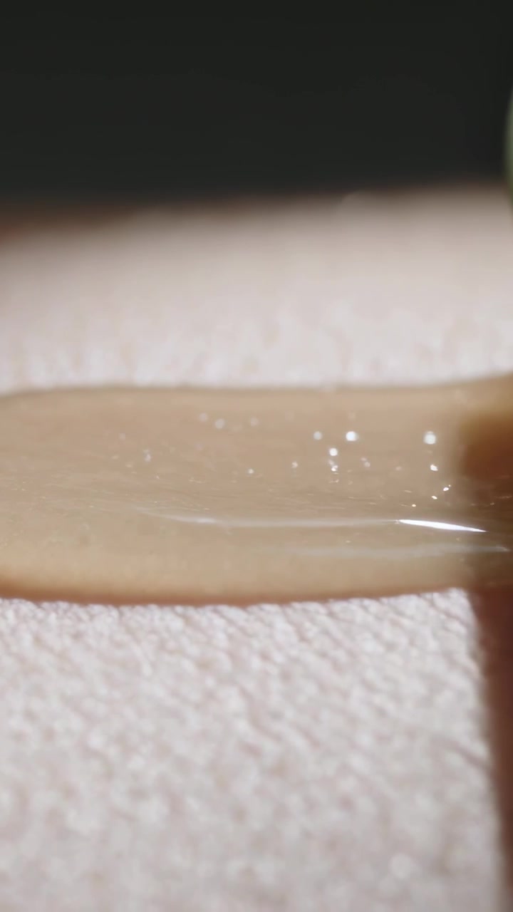 Video verticale: Anello in movimento che spinge una perla verde, trascinando del gel beige su una superficie chiara, con spazio per il testo.