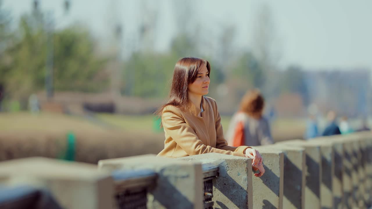 난간에서 경치를 즐기는 갈색 머리 소녀. 봄날 산책로를 따라 걷는 예쁜 여성. 카메라의 원형 움직임.