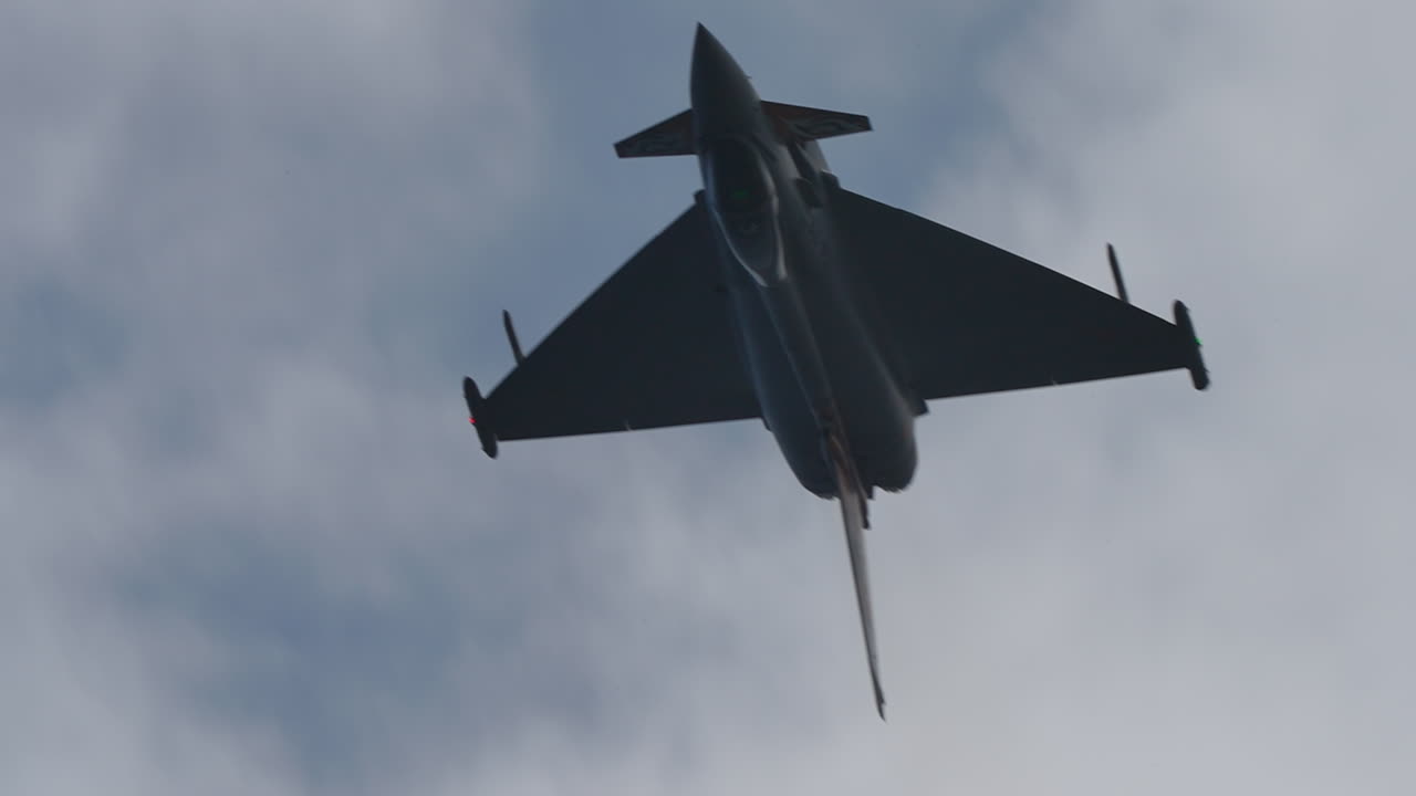 Military jet aircraft flying upside down in slow motion with visible silhouette and cloudy sky background