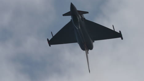 military jet aircraft flying upside down in slow motion with visible silhouette and cloudy sky background