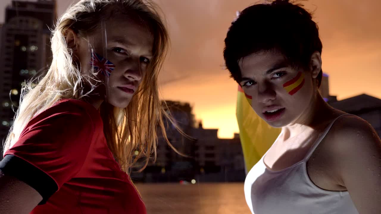 retrato de dos chicas jóvenes, aficionados al fútbol bajo la lluvia, el estadio de inglaterra y españa en el fondo 50 fps