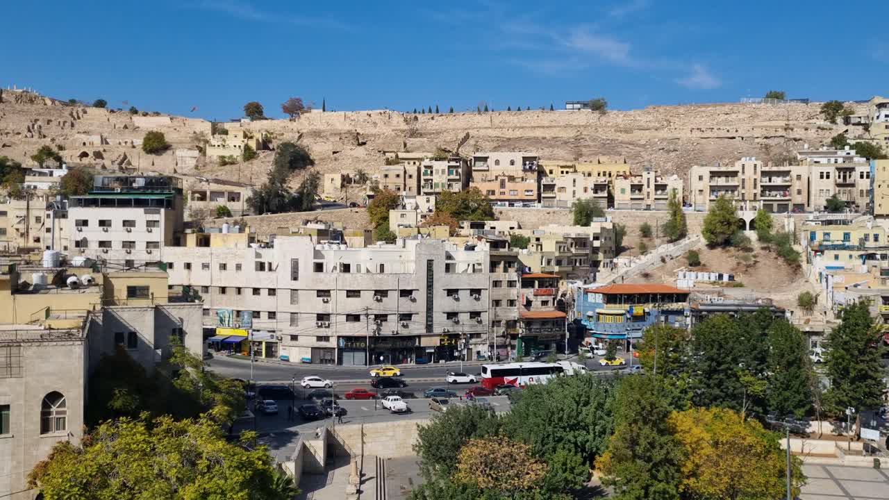 Vista sul traffico e sulle case locali sotto Jabal al-Qal'a (Collina della Cittadella) ad Amman, in Giordania, in una luminosa giornata di sole, che mostra la vita quotidiana e il ritmo urbano nella capitale mediorientale
