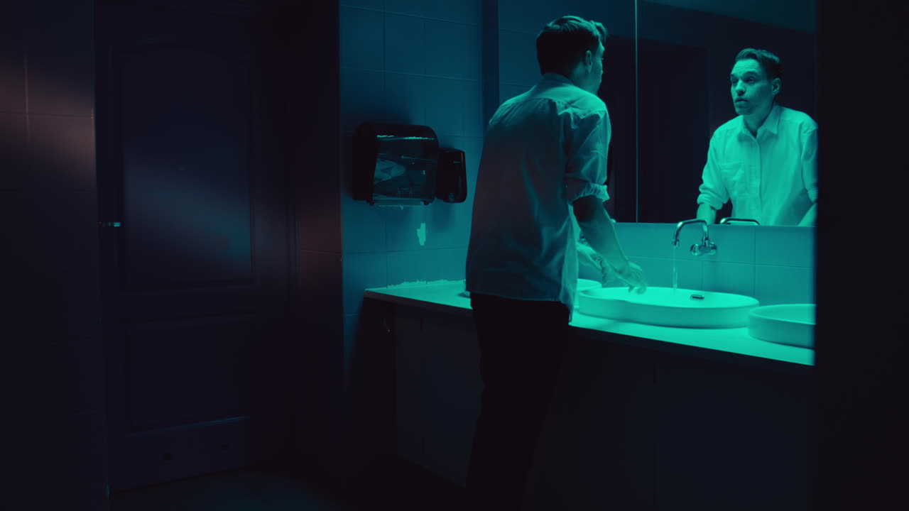 Man washing face in a bathroom at night
