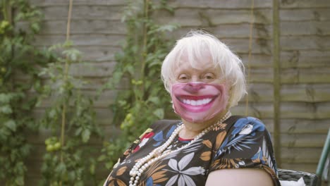 elderly woman wearing a smiley face face mask looking at the camera smiling