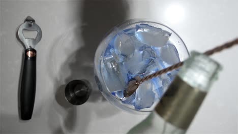 top view of a large stemmed balloon glass as a man pours in the tonic to make a refreshing pink gin and tonic cocktail