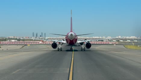 an immersive cockpit view: taxiing along a taxiway behind a commercial jet at madrid, with the city skyline at the back under a blue sky.