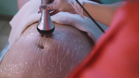 large woman client with gel on belly undergoes vibromassage