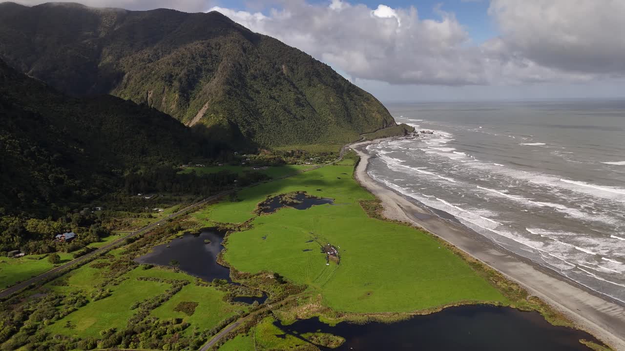 Contrasto tra la pianura costiera verde con zone umide e il mare di Tasman agitato vicino a Barrytown, Nuova Zelanda. Vista aerea dall'alto.