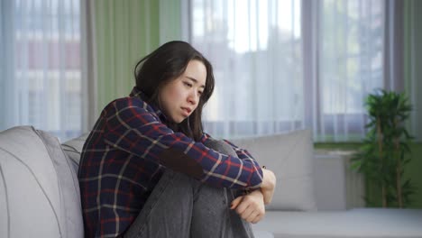 depressed and worried asian woman sitting alone on sofa at home.