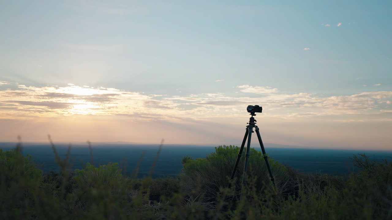 A camera on a tripod capturing a scenic sunset or sunrise landscape