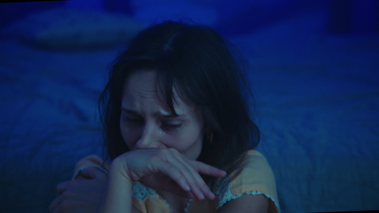 A traumatised and disoriented girl sits on the bedroom floor